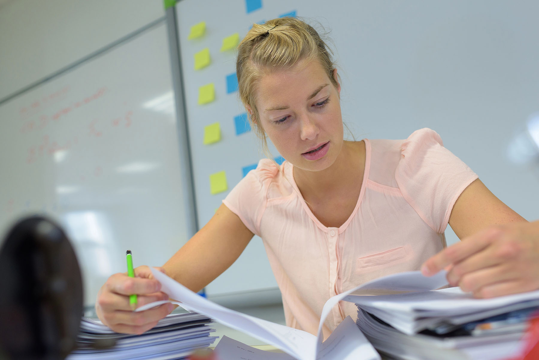 Eine junge Frau sitzt mit Stift in der Hand am Schreibtisch und arbeitet Unterlagen durch